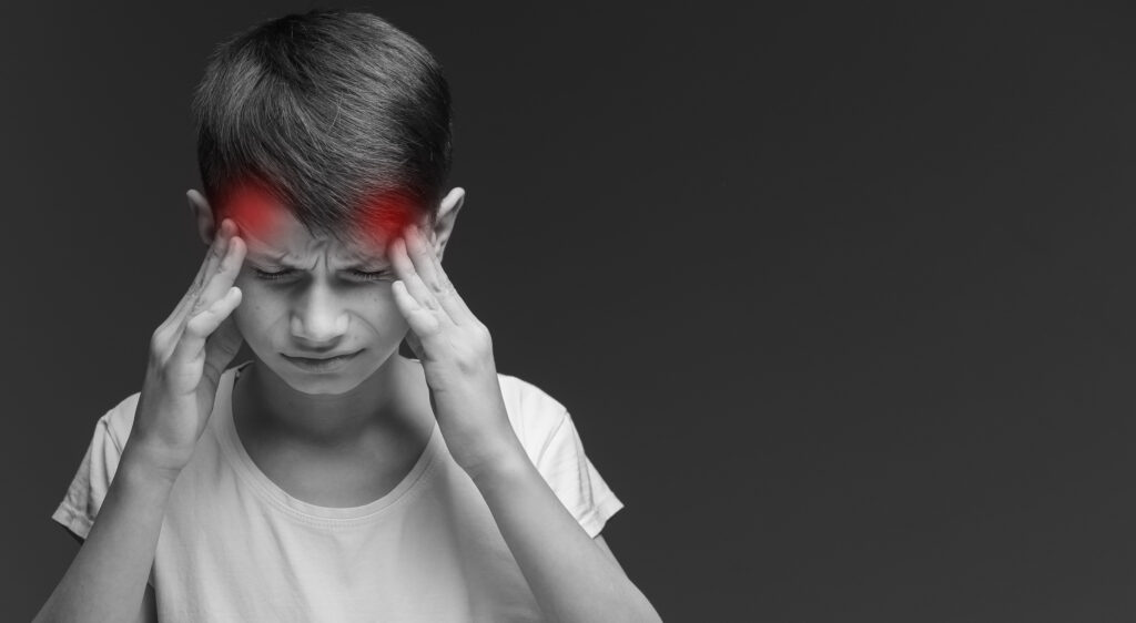 boy on grey background suffering from headache desperate and stressed because pain and migraine. Hands on head. headache in children. overload at school. pronounced red pain points on the head